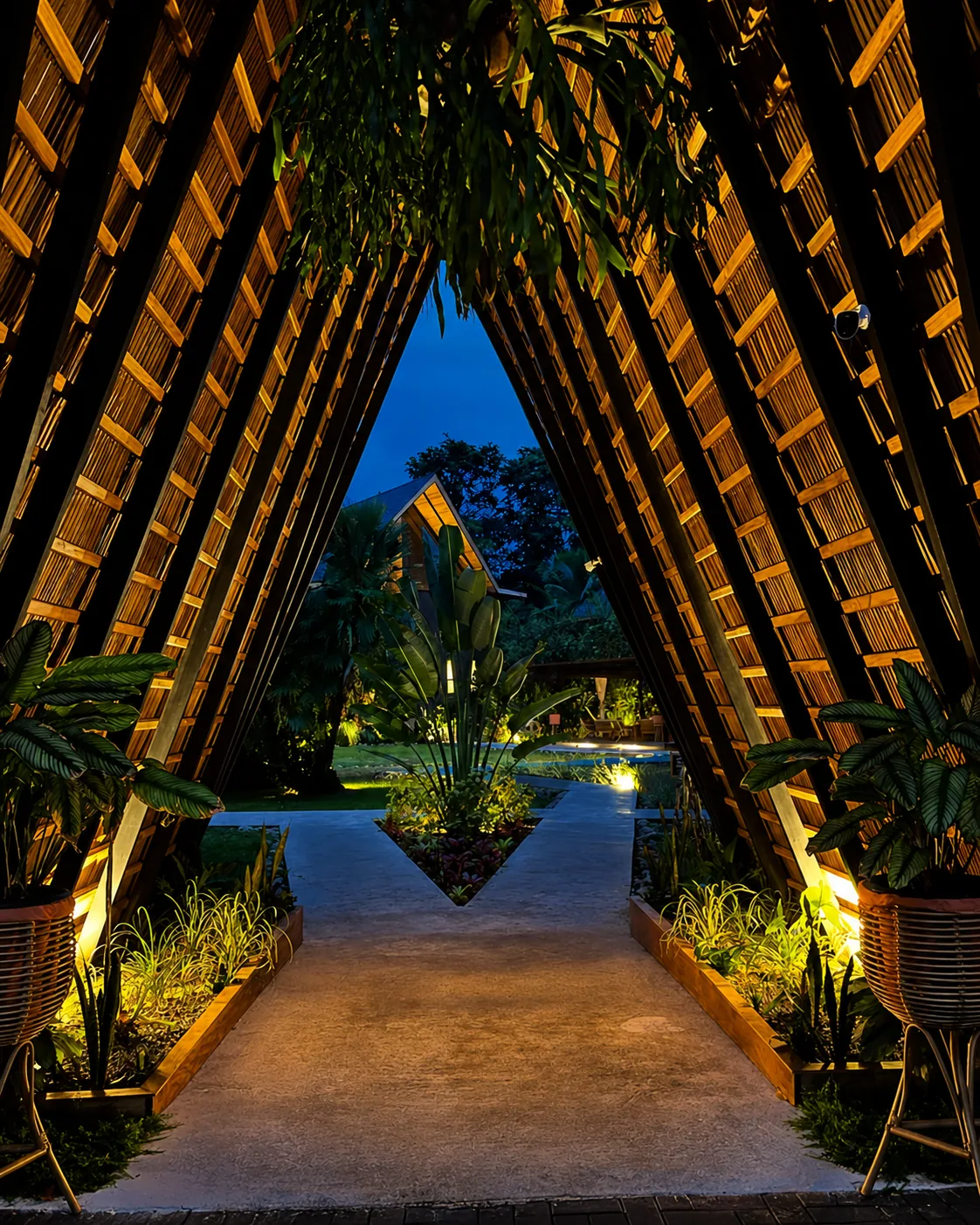Pasarela de madera iluminada entre la arquitectura triangular y el jardín de Namú